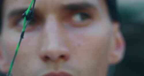 Slow motion close up of young man with professional equipment is practising archery with a bow in