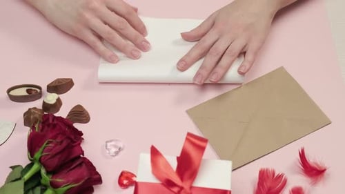 Hands Folding a Card with Valentine's Gifts