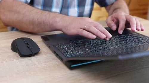 23Close-up of hands using a laptop keyboard and mouse on a wooden desk. Work, internet browsing, and