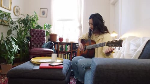 Woman plays acoustic guitar on the couch