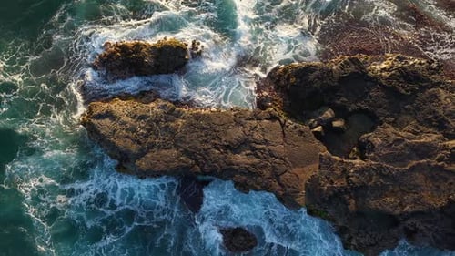 A Topdown Aerial View of Powerful Ocean Waves Crashing on Volcanic Rocks in Cinematic Slow Motion