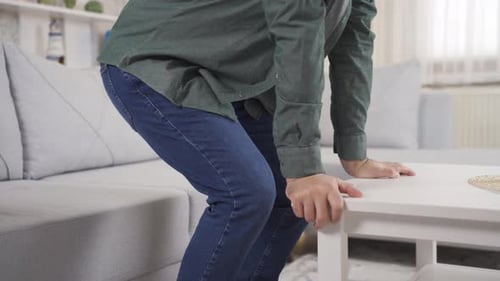 Man with sore knees is having trouble sitting on sofa at home. Joint pains.