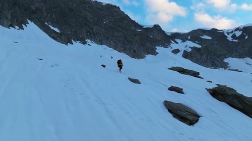 Luftaufnahme: Männlicher Bergsteiger, der auf einem steilen Schneefeld mit Felsen und Berghintergrund läuft