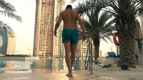 Young man enters swimming pool in super slow motion at city resort