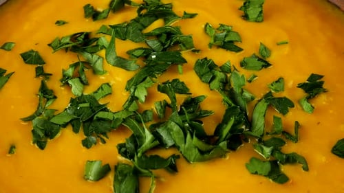 Chopped parsley falls into a clay bowl with pureed pumpkin soup.