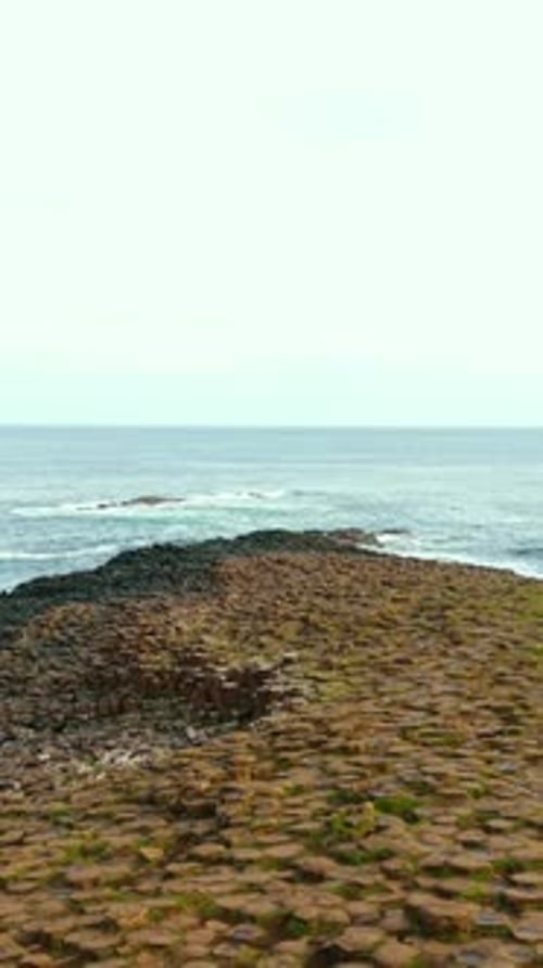 Low reversing social ratio aerial video of The Giant's Causeway in Bushmills, Northern Ireland