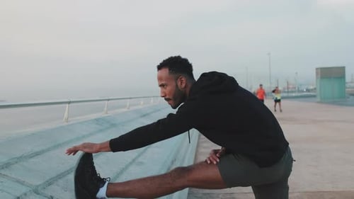 Man Stretching Leg on Promenade in Urban Setting