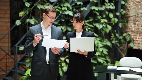 Business Colleagues Discuss a Project Using Documents and a Laptop in a Modern Office