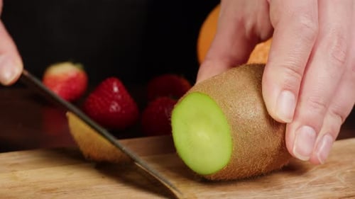 Slicing Kiwi Fruit with Knife on Cutting Board