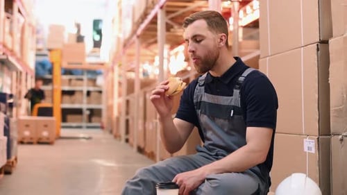 Lunch time. Eating and drinking. Storage worker in uniform is in the warehouse