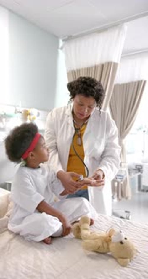 Vertical video of african american female doctor with stethoscope examining a girl at hospital