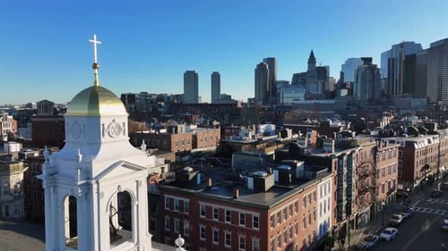 Golden dome crowns St. Leonard’s Church in Boston’s North End. Skyline rises behind brick rowhouses.