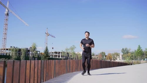 Young adult asian runner jogging down the street. Нandsome man in a sports suit is doing a daily run