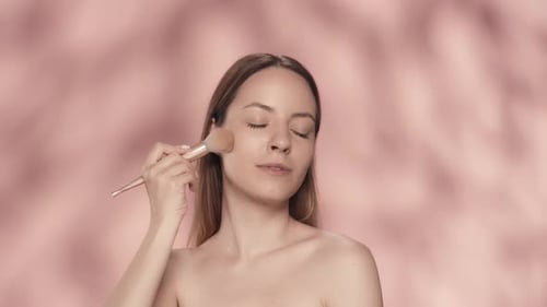 Seminude Woman Uses a Makeup Brush in the Studio on a Pink Background Close Up A Woman Does