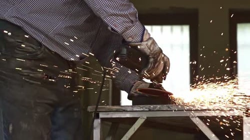 Slow motion shot of a worker grinding metal with an angle grinder, producing bright sparks in an ind