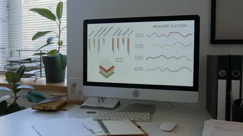 Office Desk with Computer Displaying Business Metrics on Screen