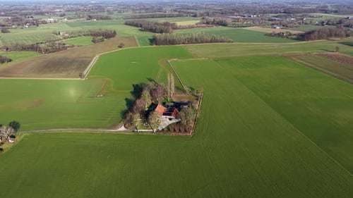 Eine Drohnenaufnahme eines traditionellen Bauernhauses mit roten Dächern, umgeben von üppigen grünen Feldern.