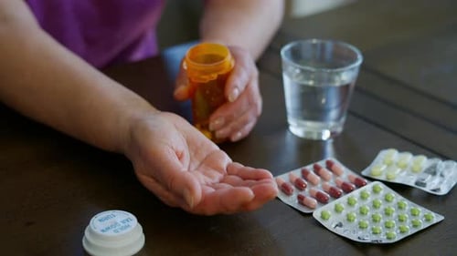 Close Up of Elderly Hands Pouring Pills From an Orange Prescription Bottle Into the Palm with