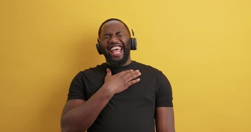 Overjoyed dark skinned man with headphones laughs hears funny story on yellow background