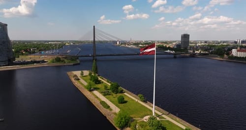 Drone Ascends Above Latvian Flag, River Daugava and Vansu Bridge