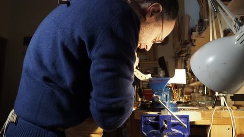 Bent-over luthier hand-carving a violin scroll under bright workshop light with artisan precision