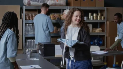 Young Woman Taking Uniform and Badge at Donation Center with Diverse Volunteers