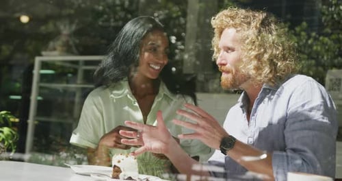 Happy diverse couple sitting at table and talking in cafe