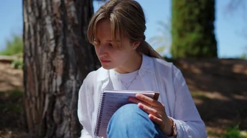 Young Woman Writing in Notebook Under a Tree