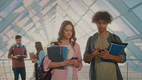 Two Students Talking and Using Smartphone in the College Hallway