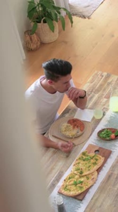Vertical video: Eating hungry man bringing forkfuls from plate sipping drink tucking napkin at home