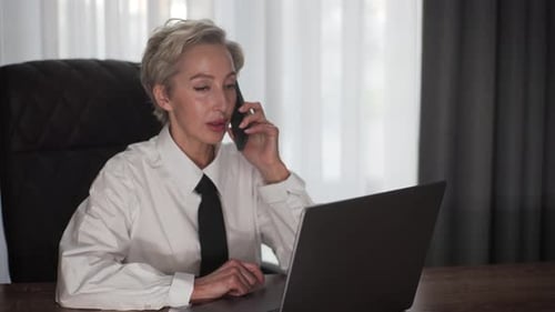 Elegant Middleaged Business Woman Talking on Smartphone Siting at Office Workplace Desk Share