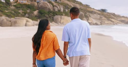 Couple, beach and walking while holding hands outdoor and happy together on vacation or holiday