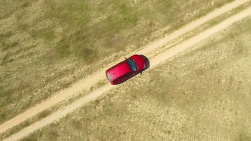 A car drives through the ruts of a dusty dirt road across wild deserts fields.