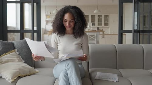 Young Woman Reviews Papers at Home on Sofa