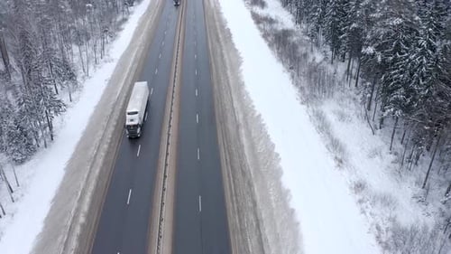 A white truck drives along the road among snowy trees in winter