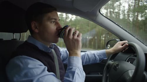 A Man Drives a Car and Drinks Coffee