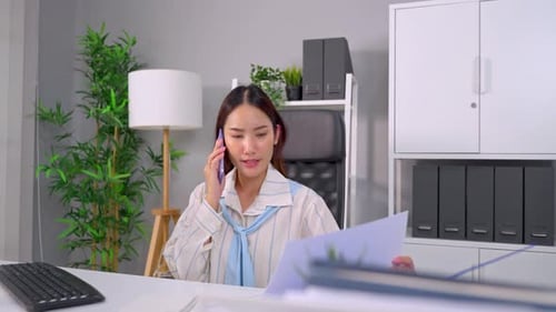 Asian young businesswoman talking on smartphone and working in office