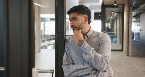 Thinking deeply, businessman standing in modern office hallway