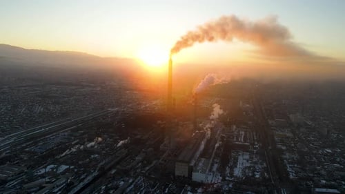 Industrial smokestacks emitting pollution over a hazy city at sunset