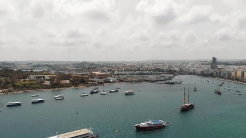 Aerial 4k drone footage panning from a harbor with anchored sea vessels and revealing a cityscape of