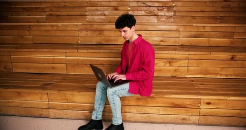 Man Works on Laptop Sitting on Wooden Bench
