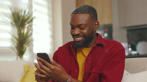 Man Smiling While Using Cellphone on Sofa