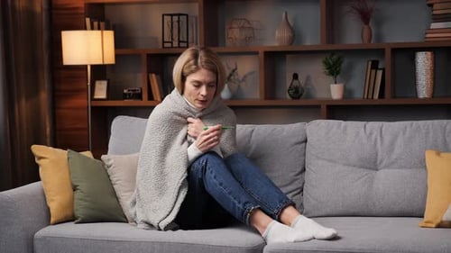 Femme malade et malade enveloppée dans un plaid tricoté chaud tremblant avec froid, assise seule