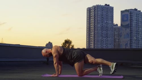On the Roof Overlooking the City a Wellbuilt Man is Doing Sports