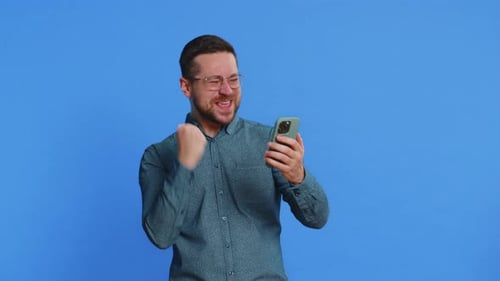 Excited man celebrating success while using smartphone