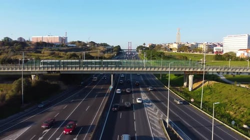 Drone shot focusing on an Urban Train crossing a bridge right over a highway with Lisbon Portugal