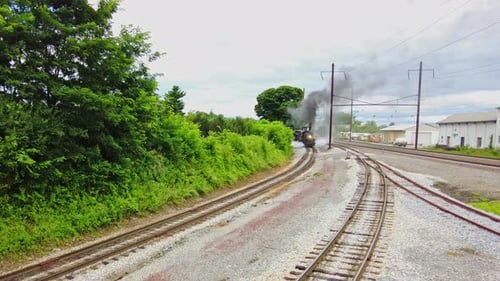 An Elevated View of a Large Steam Engine Passenger Train Blowing Smoke Passing on a Siding on a Clou