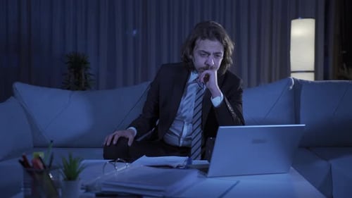 Man Looks Tired Working Late on Laptop at Home