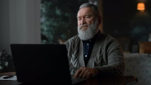 Senior Man Uses Laptop at Home Table