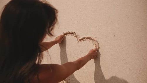Frau zeichnet ein Herz in den Sand an einem sonnigen Strand